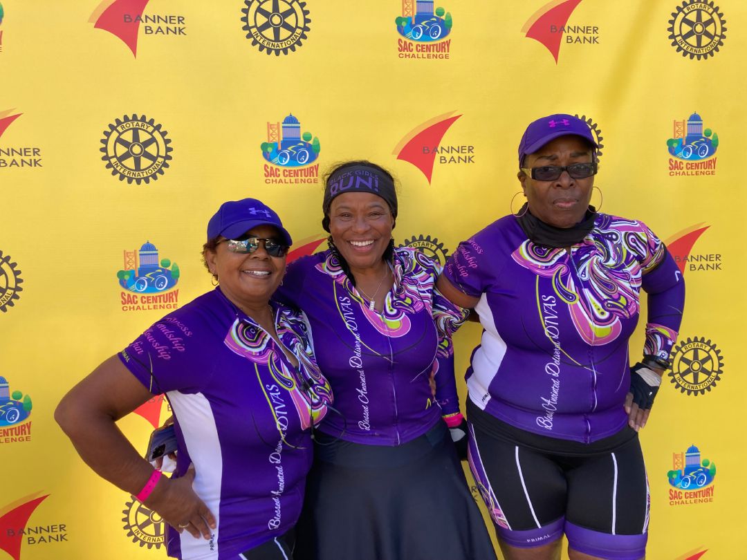 Three female riders in purple jerseys posing in front of backdrop